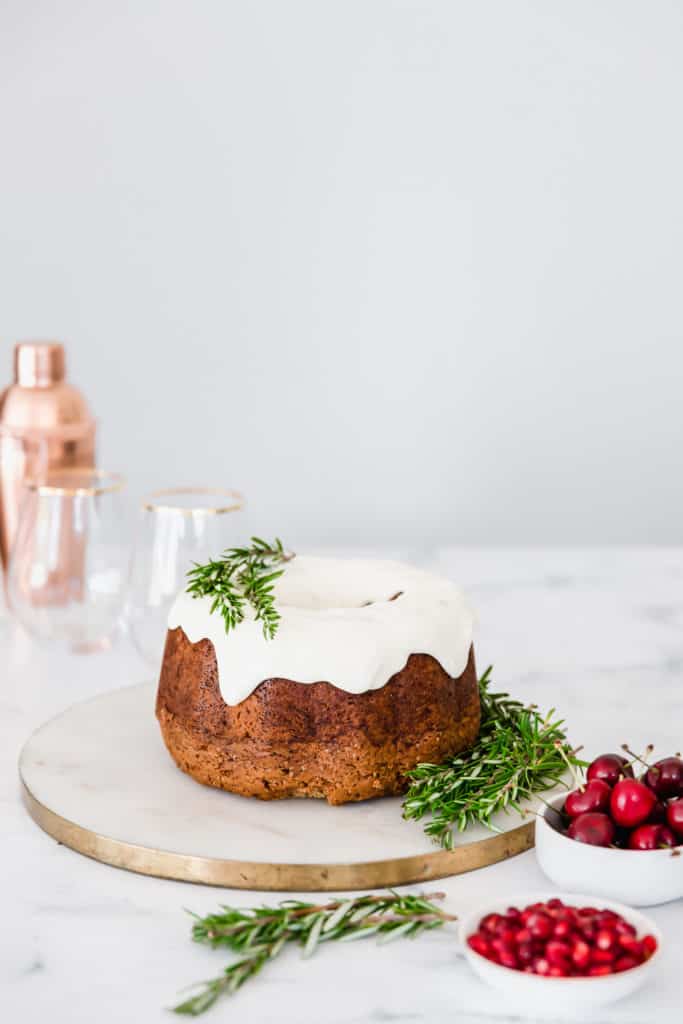 A bundt cake surrounded by fresh rosemary and berries.