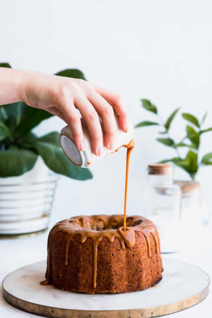 A bundt cake with a hand pouring butterscotch glaze out a jug.