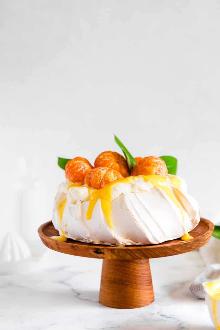 Clementine winter pavlova with curd and whipped cream on a wooden cake stand.