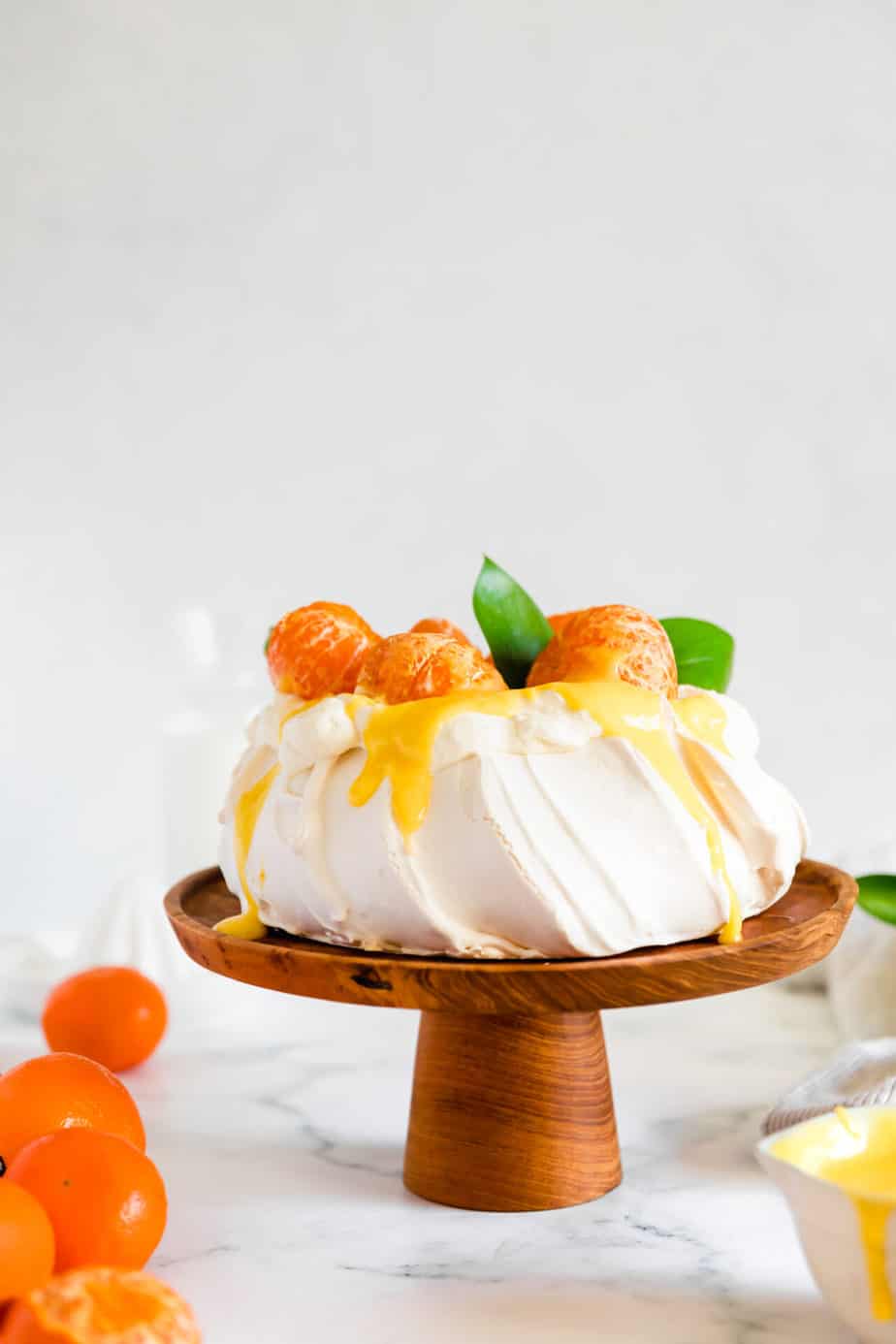Clementine winter pavlova with curd and whipped cream on a wooden cake stand.