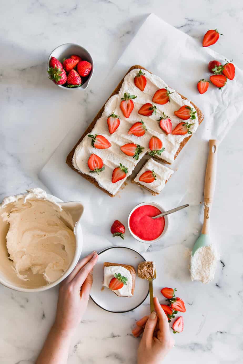 A sheet cake with a bowl of strawberry lemon buttercream and fresh strawberries.
