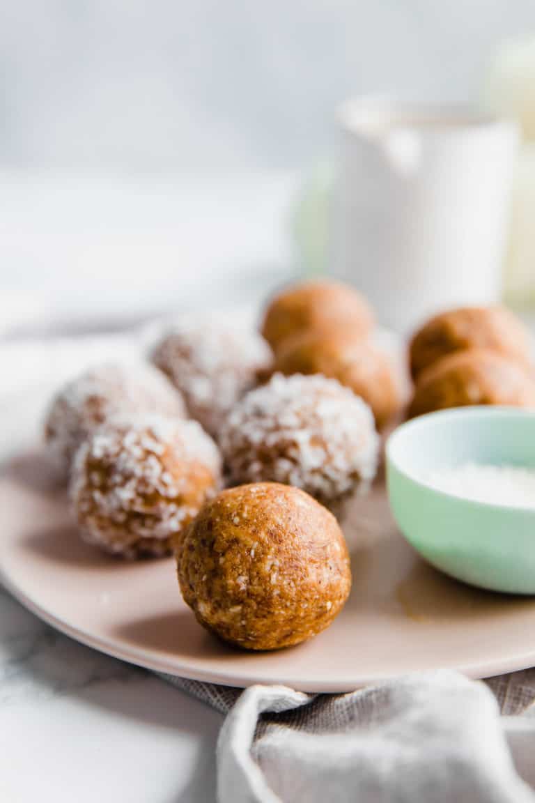 Coconut covered healthy bliss balls on a pale pink plate.