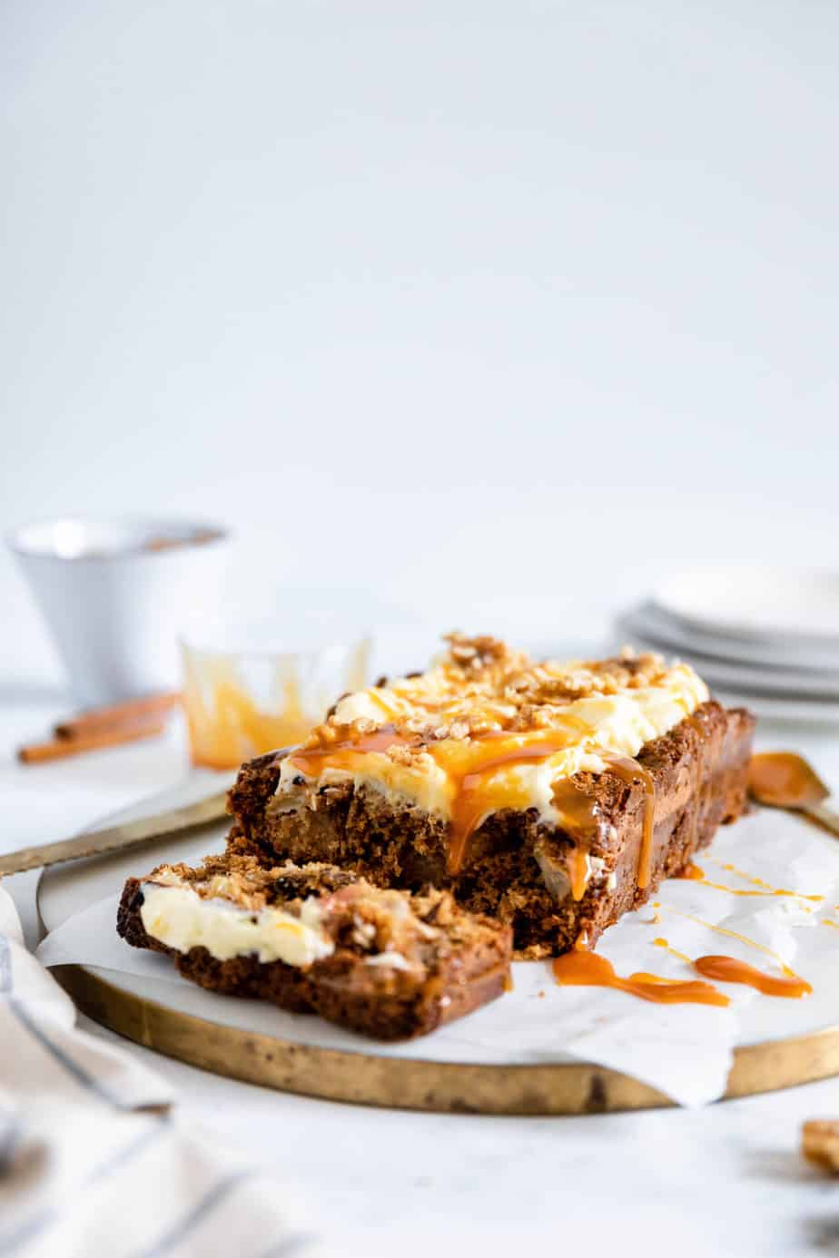 A apple and walnut loaf topped with creamy frosting and a drizzle of caramel sauce.