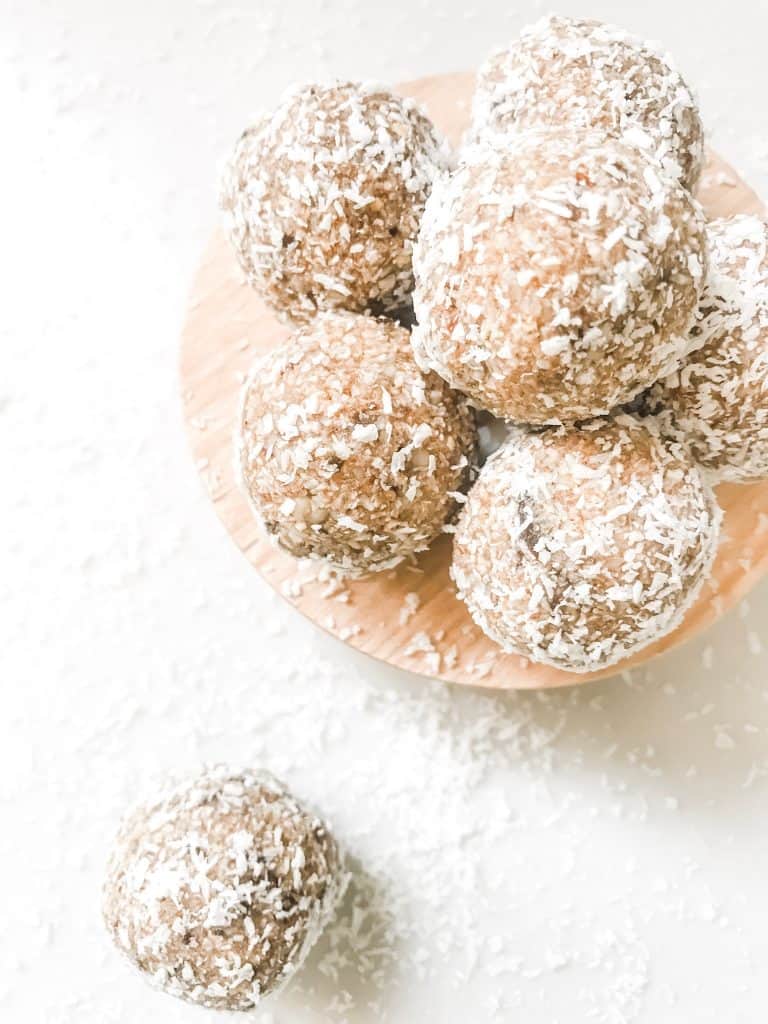 Healthy energy bliss balls on a wooden plate with a sprinkle of coconut.
