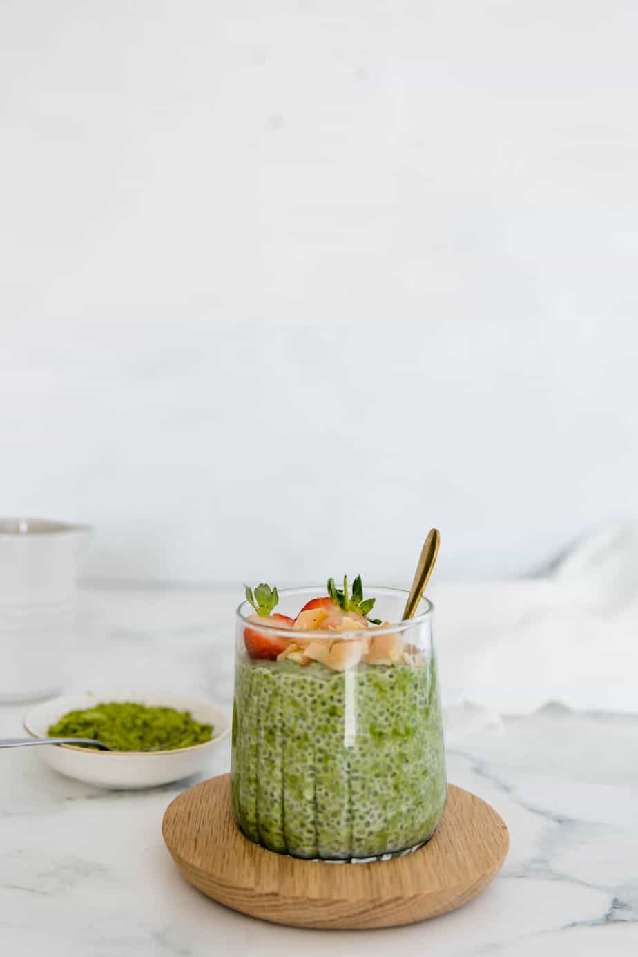 Matcha chia pudding with fresh strawberries in a serving glass with a gold spoon.