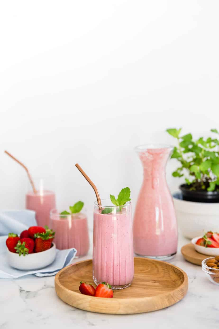 A smoothie in a glass serving glass with a copper straw on a wooden board.