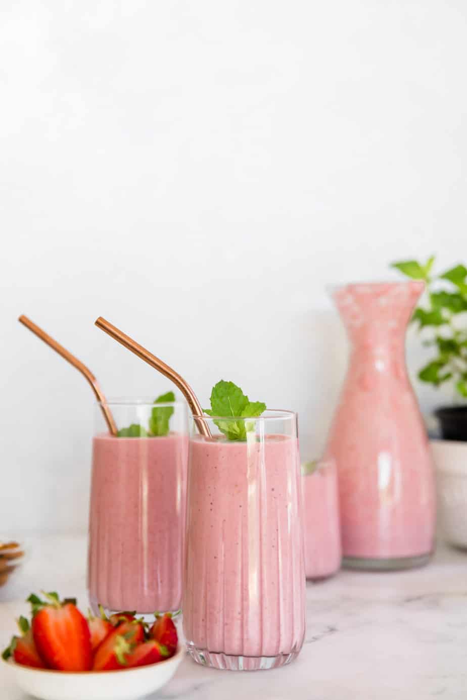 Smoothies in serving glasses with fresh strawberries.