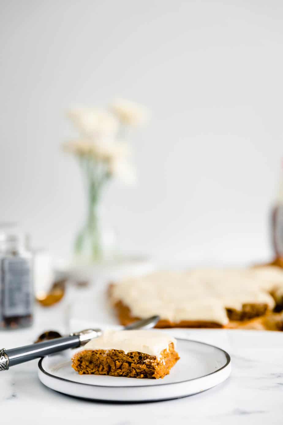 A slice of pumpkin spice sheet cake topped with frosting on a white plate.