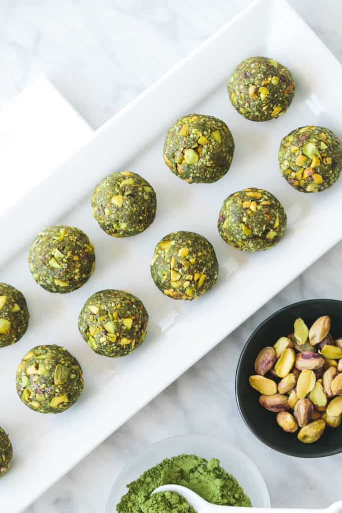 Green matcha energy balls on a white rectangular plate with pistachios.