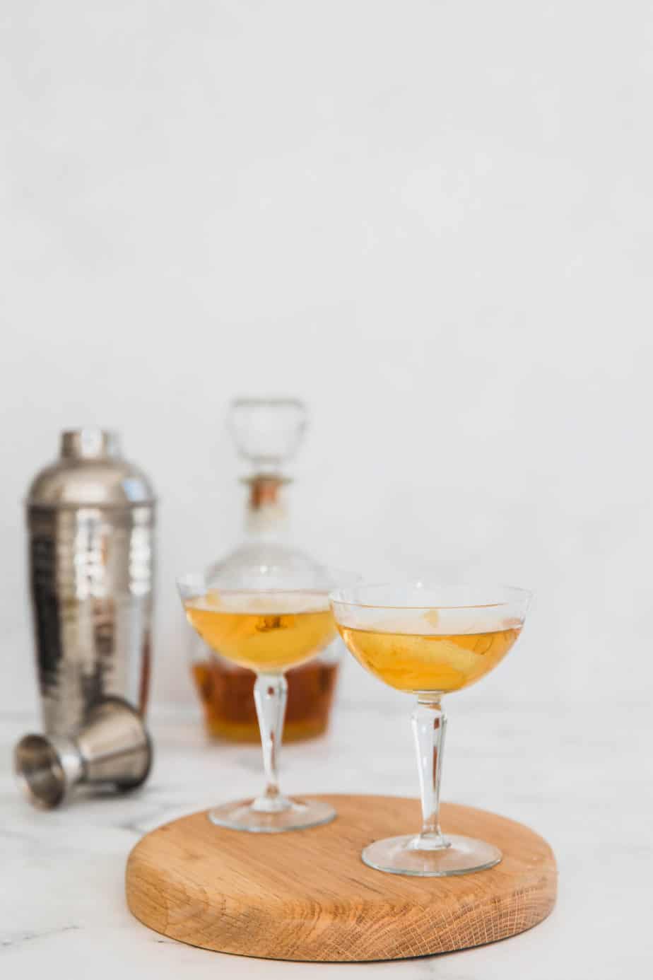 Two bourbon cocktails in serving glasses on a wooden board.