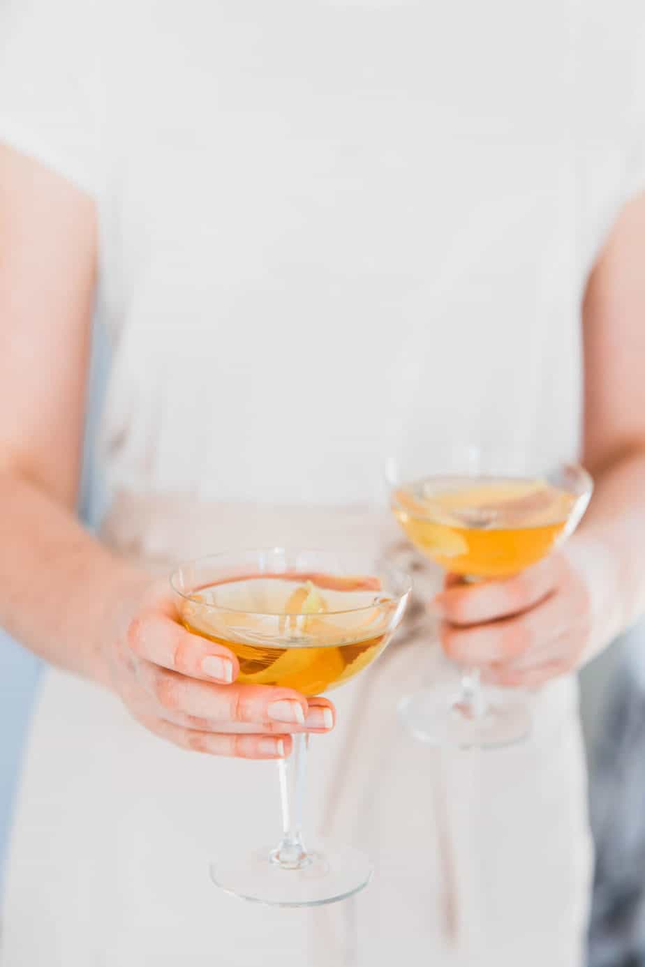 A person holding to glasses of bourbon.