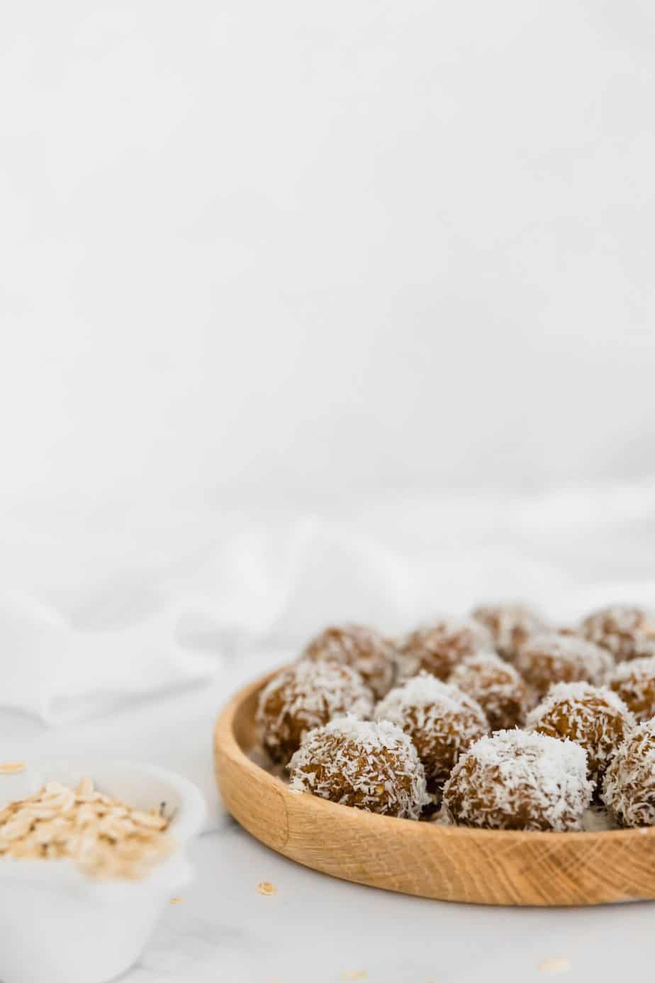 A wooden plate filled with healthy bliss balls coated in coconut.