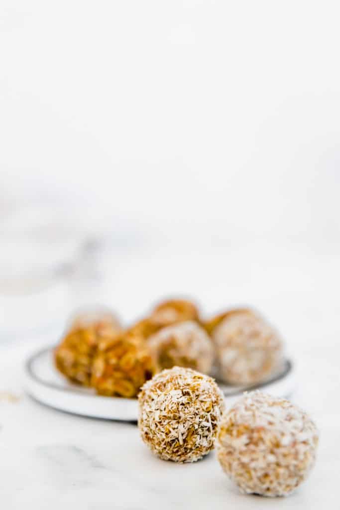 carrot cake energy balls without dates rolled in coconut on white plate 
