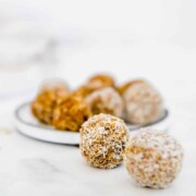 Several carrot cake protein balls rolled in desiccated coconut sitting on a marble counter.
