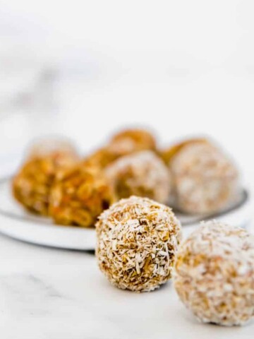 Several carrot cake protein balls rolled in desiccated coconut sitting on a marble counter.