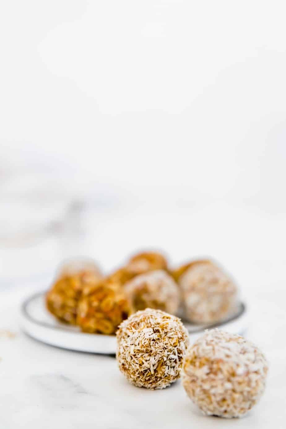 carrot cake energy balls without dates rolled in coconut on white plate 