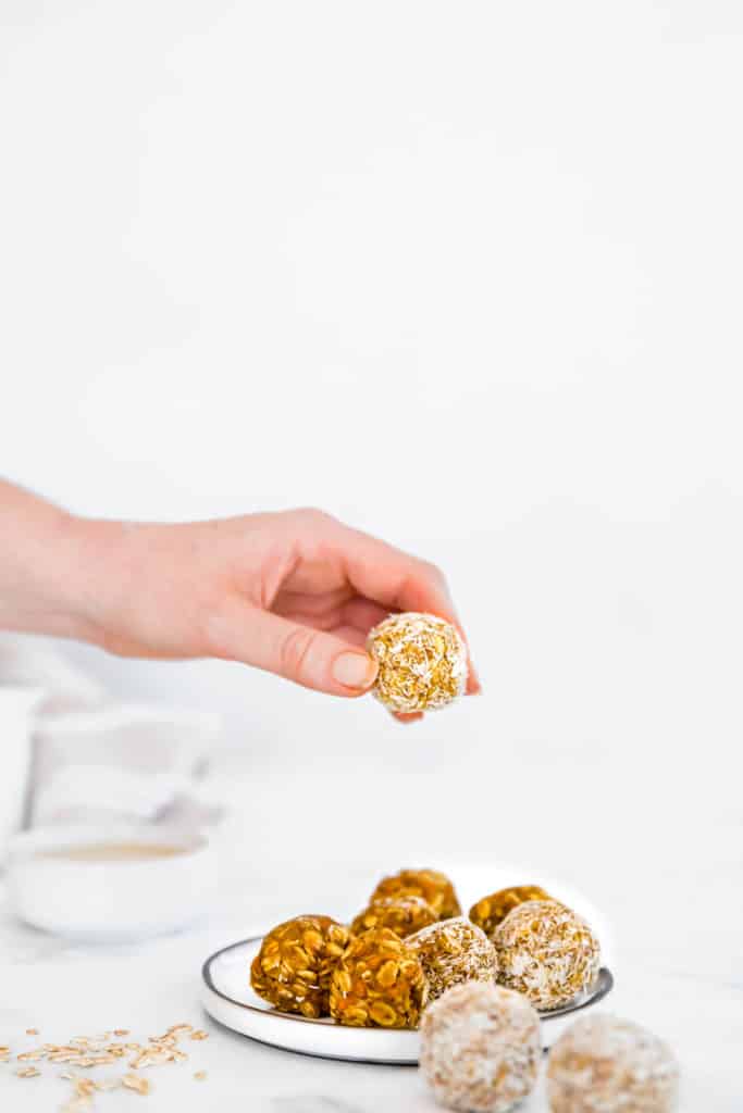 carrot cake energy balls without dates in coconut on plate with white background