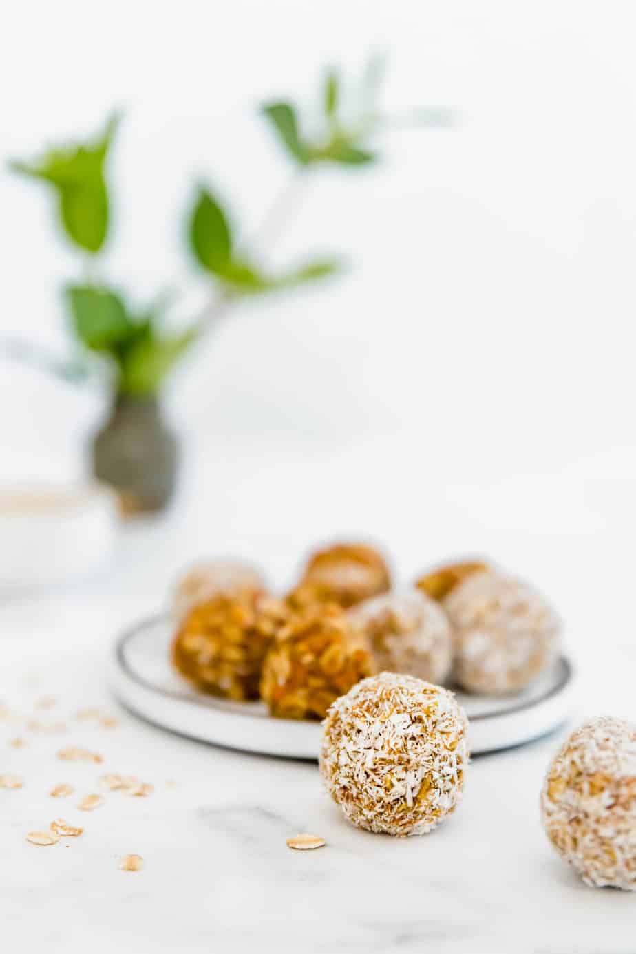 Carrot-based energy bites on a white plate with oat flakes.