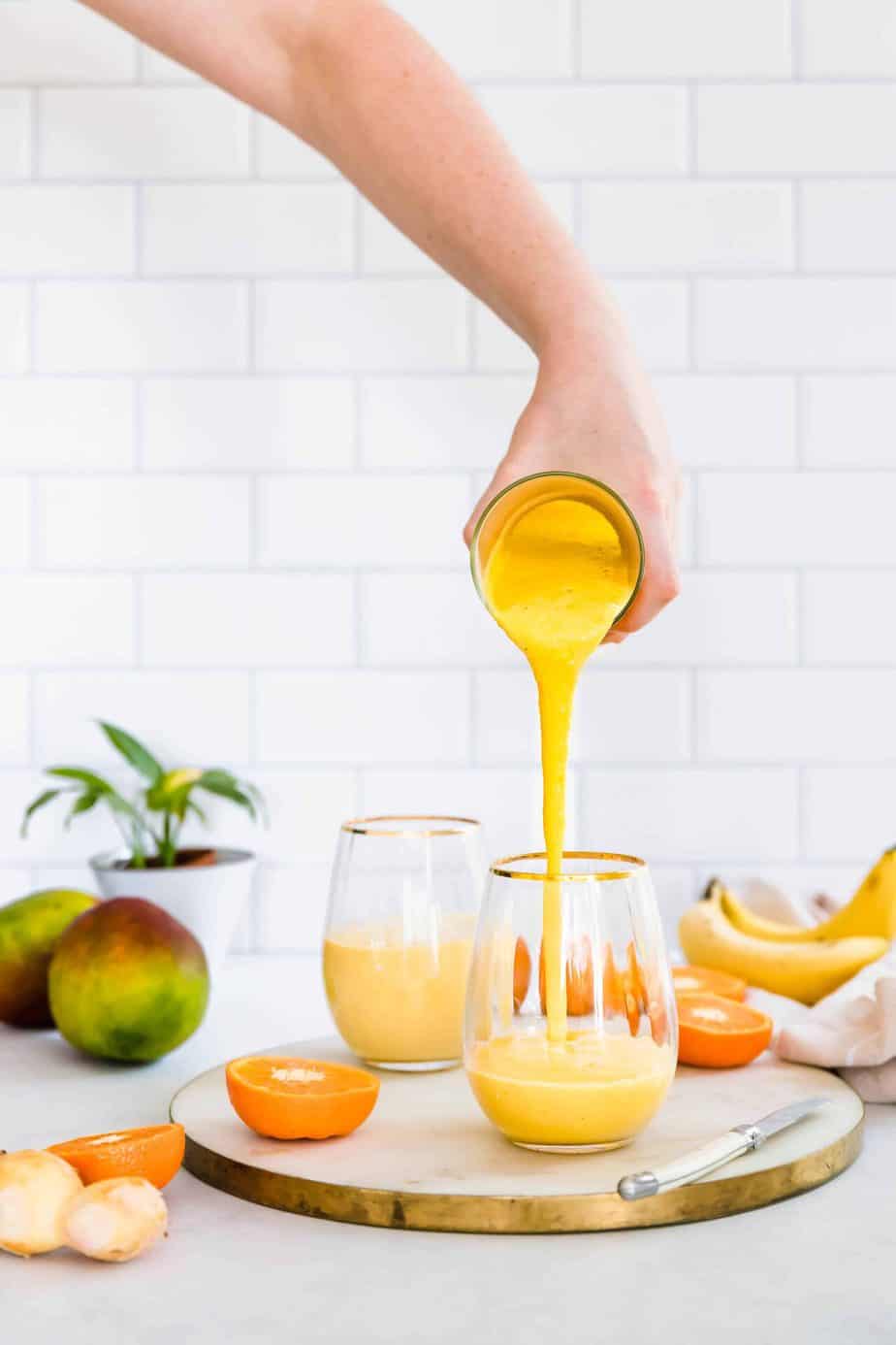 Mango smoothie pouring into a serving glass with fresh fruit.