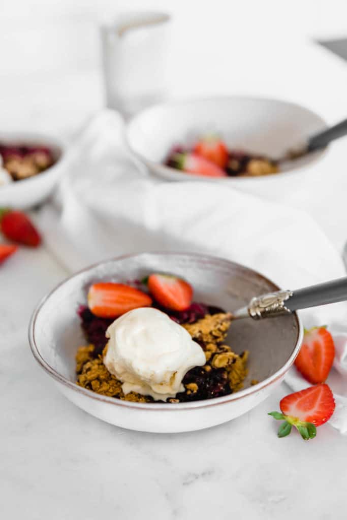 A bowl of mixed berry crumble topped with a scoop of ice cream and fresh strawberries.