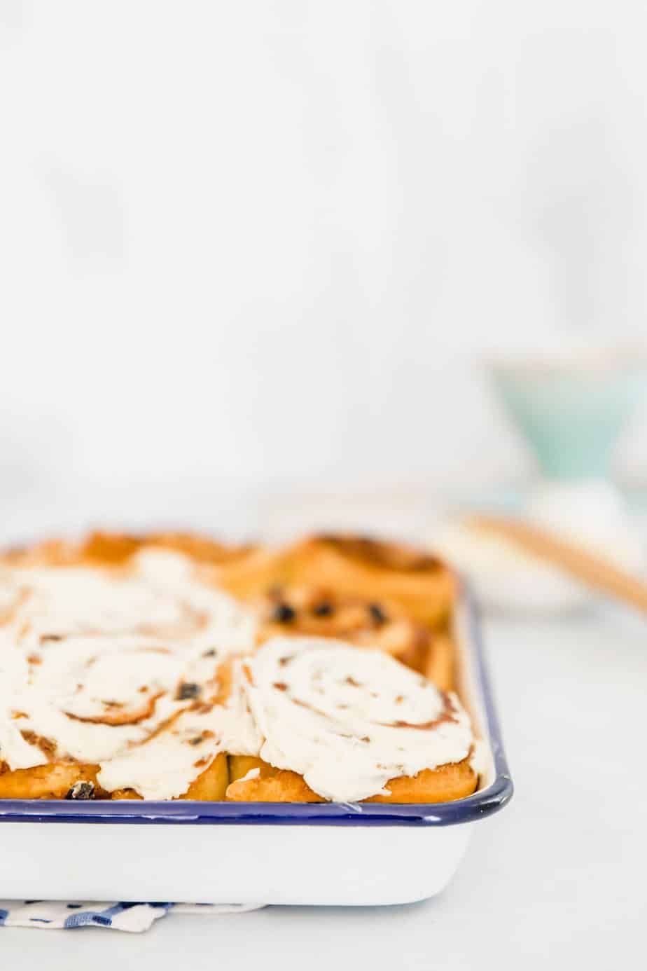 A white baking tray of cinnamon rolls with frosting on top.
