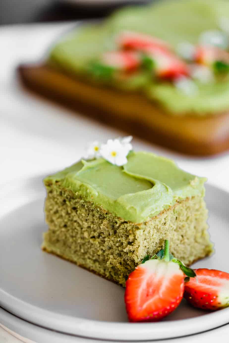 A square of matcha sheet cake with strawberries on a grey plate.