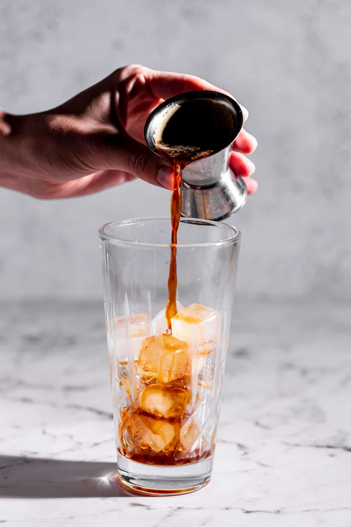 Espresso pouring into a cocktail shaker filled with ice.