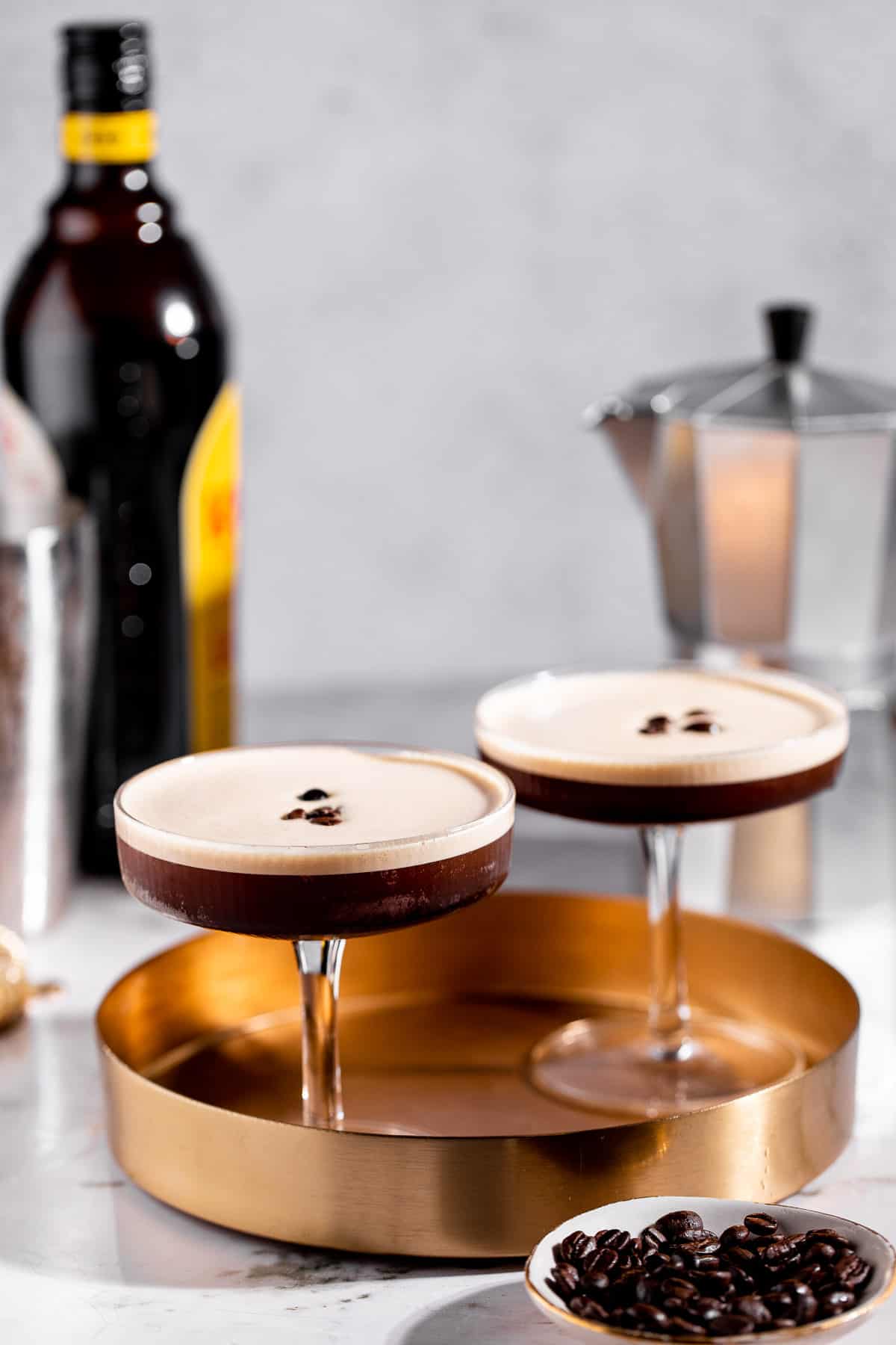 Two tequila espresso martinis on a gold tray garnished with coffee beans.