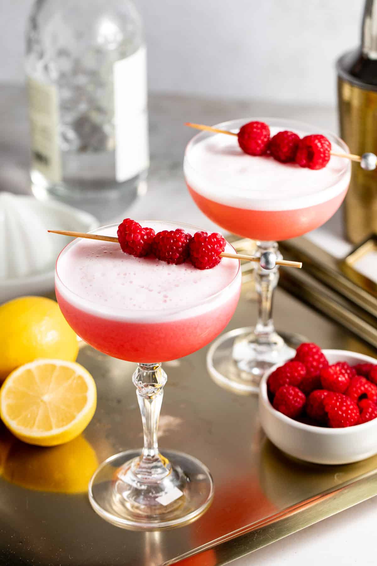 two coupe glasses on gold tray with raspberries and lemons