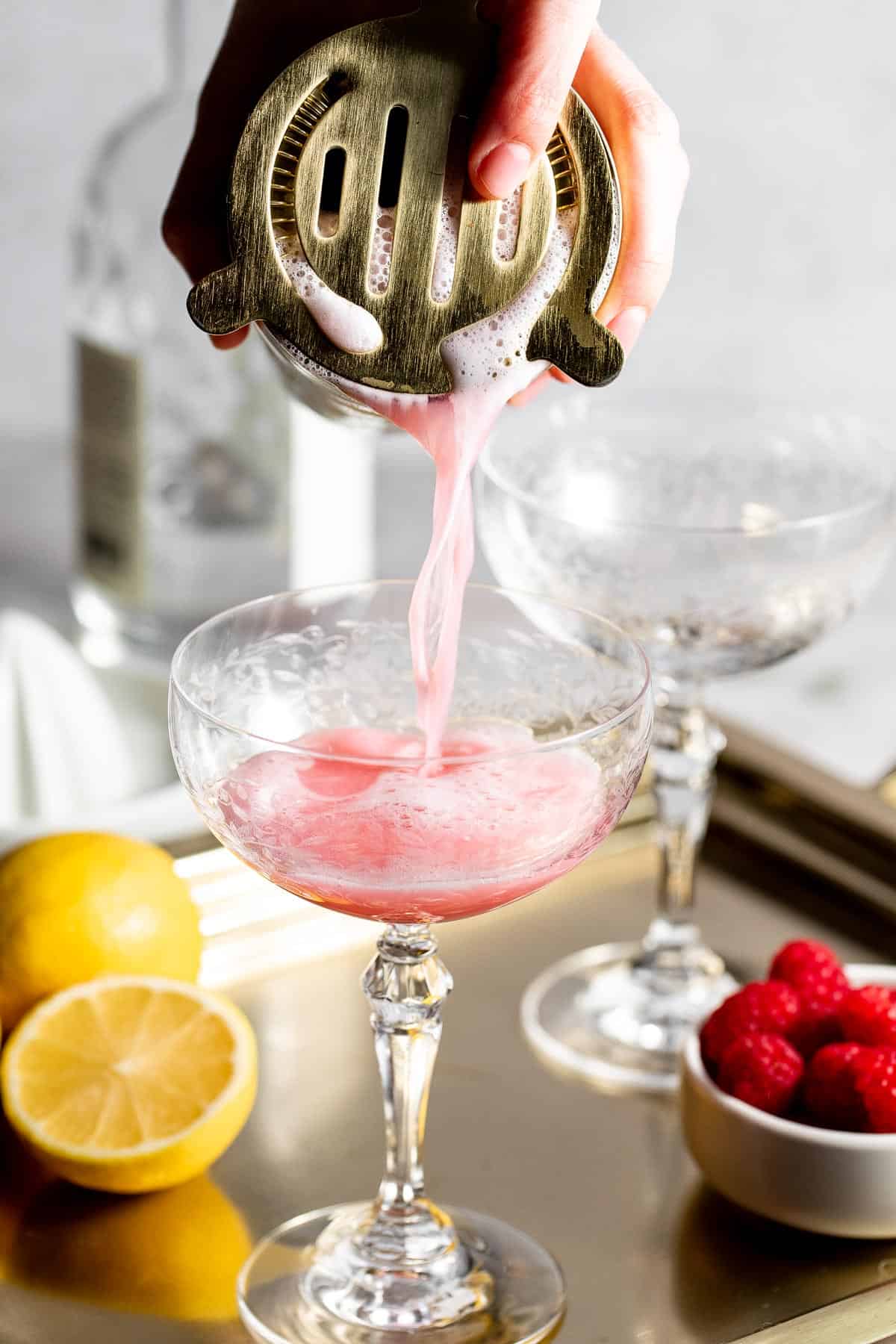 pouring clover club cocktail into coupe glass