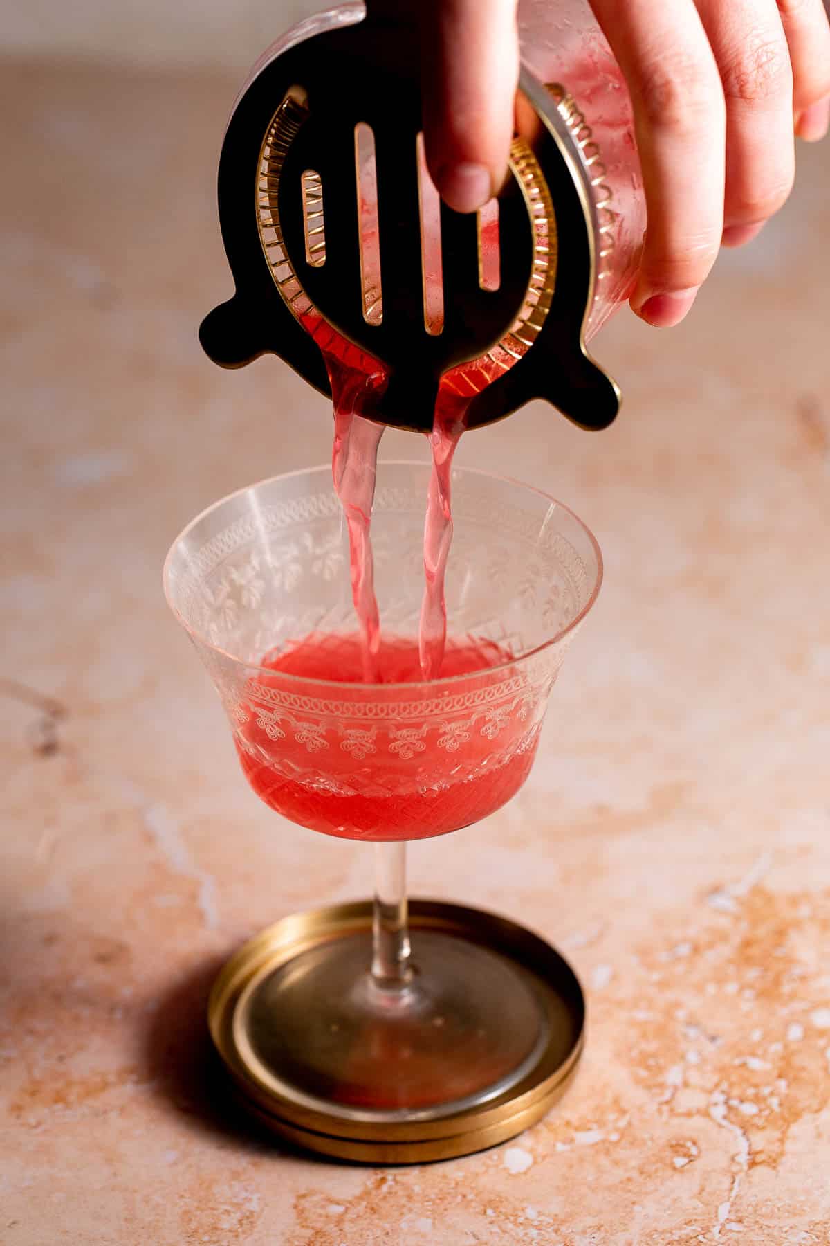 A red cocktail being strained into a cocktail glass.