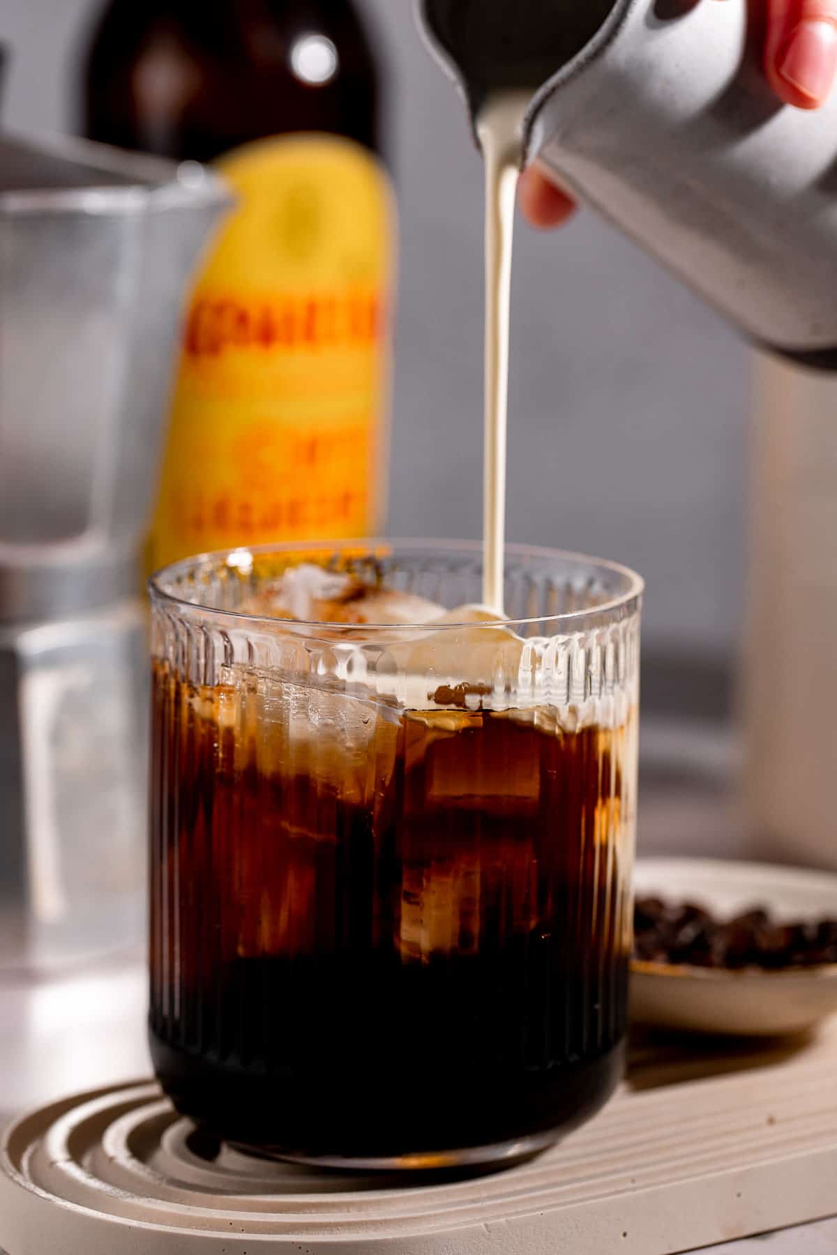 Cream pouring into a coffee cocktail filled with ice.