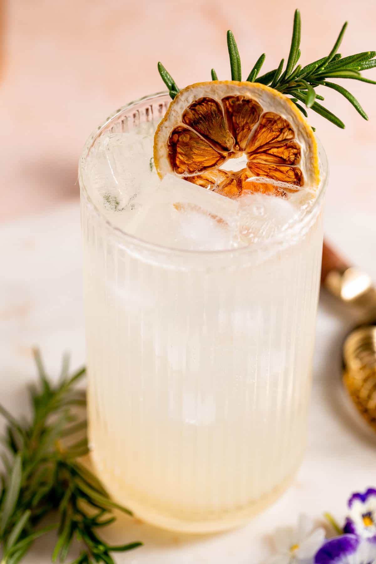 A Vodka Collins cocktail in a serving glass garnished with an orange slice and fresh herbs.