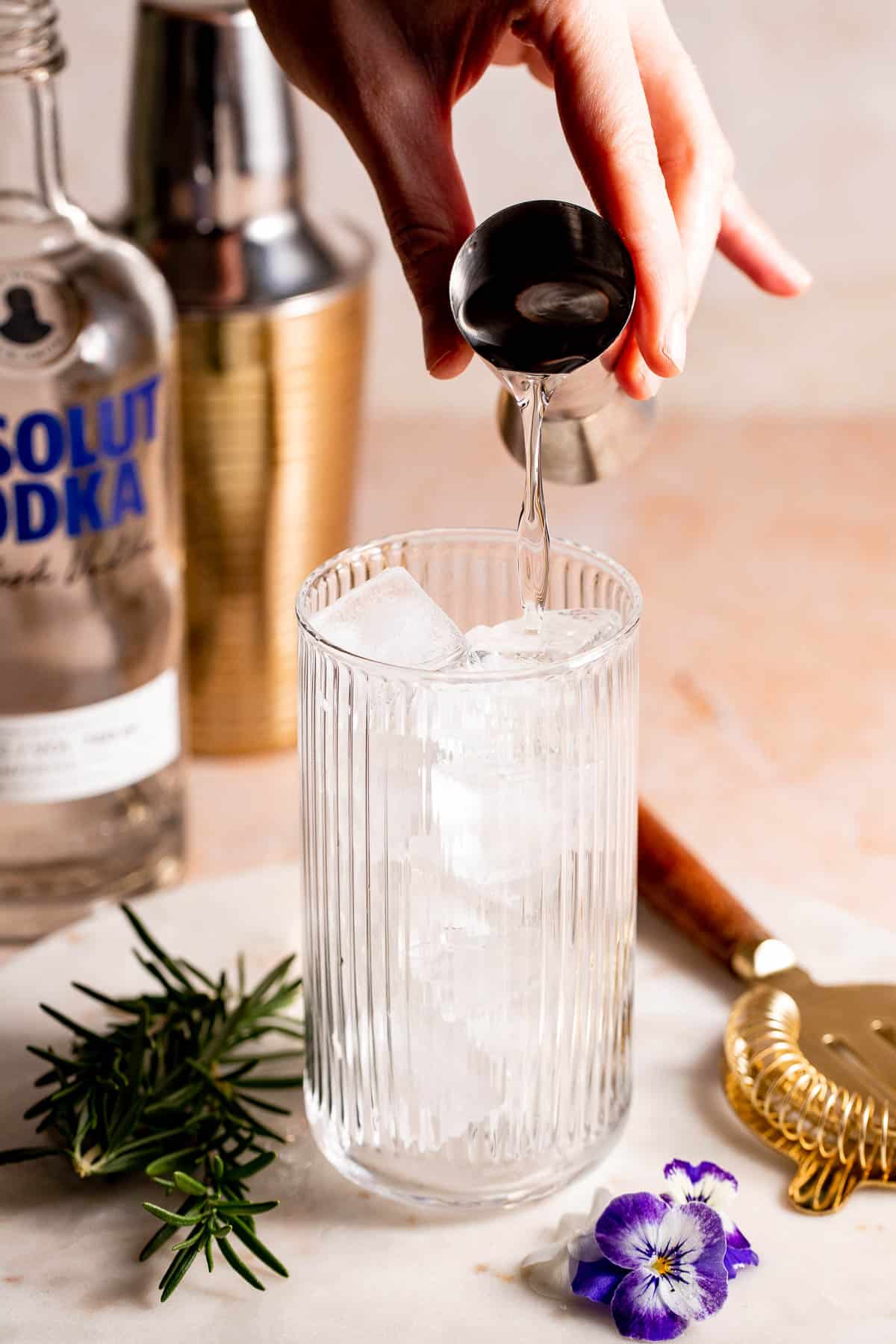 A highball glass filled with ice with vodka pouring into it