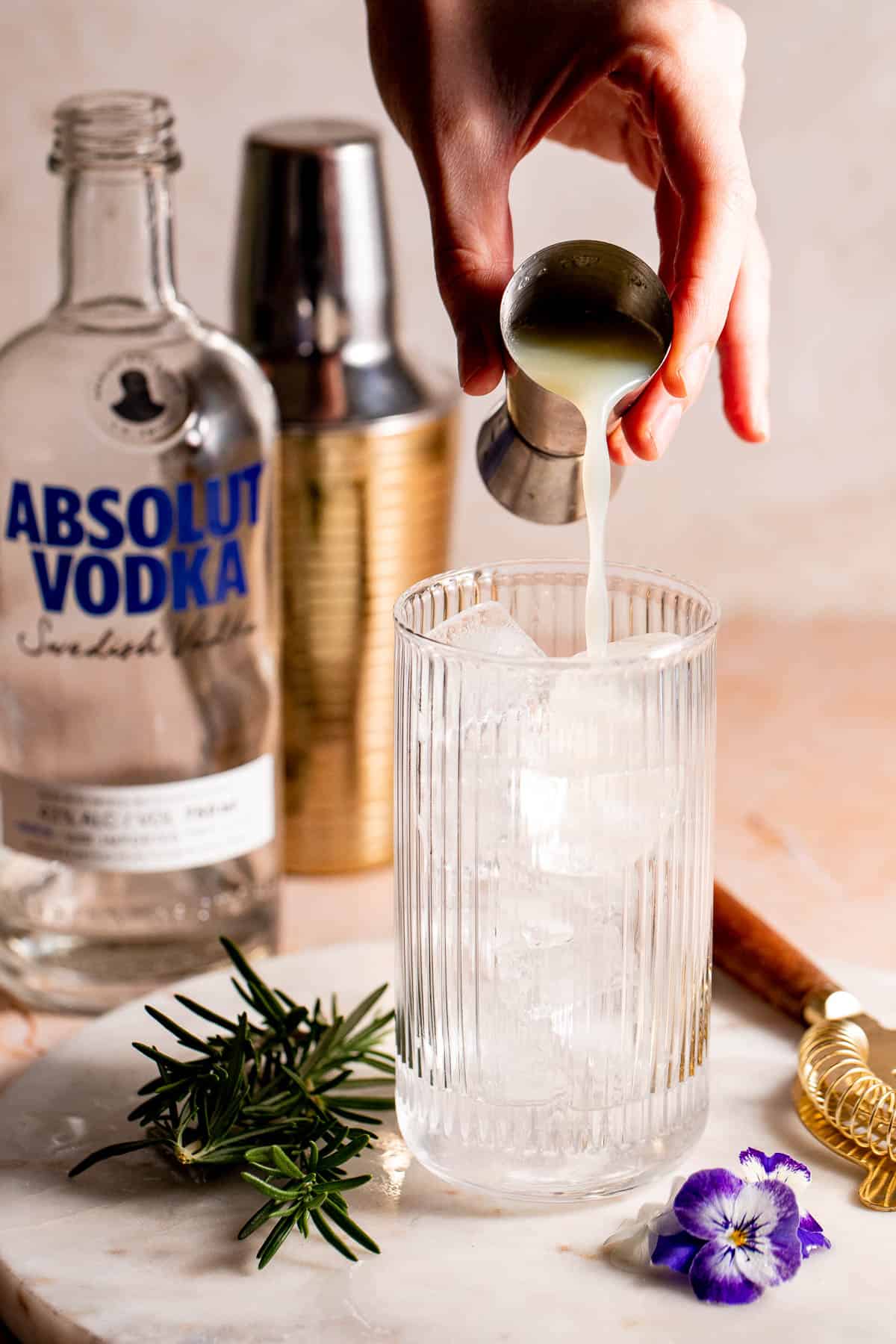 A highball glass filled with ice with lemon juice pouring into it