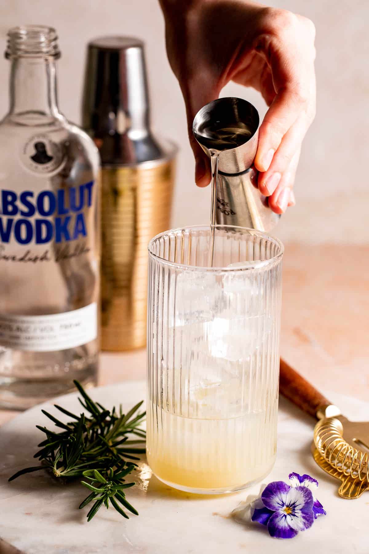 A highball glass filled with ice with simple syrup pouring into it