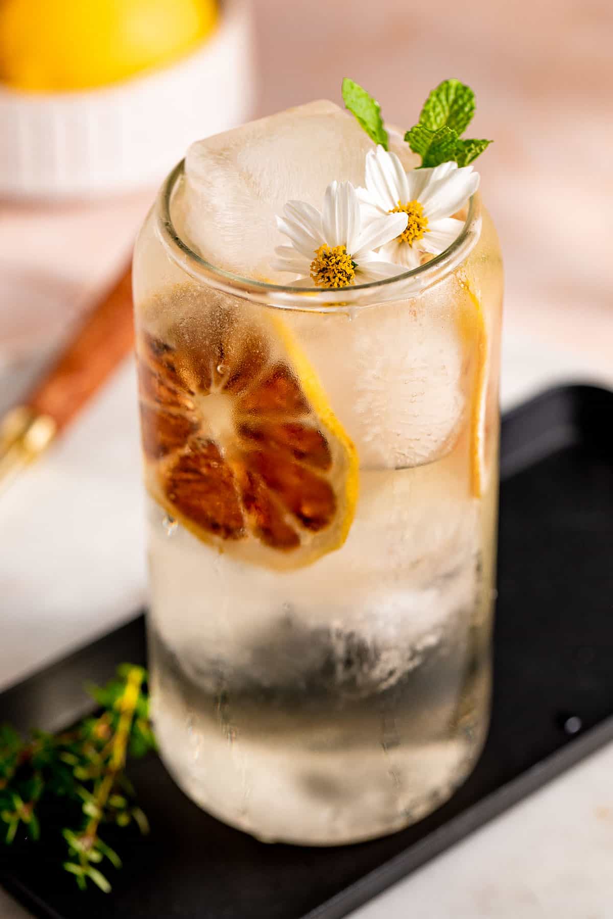 A Whiskey Highball on a black tray served with ice and fresh flowers and herbs.
