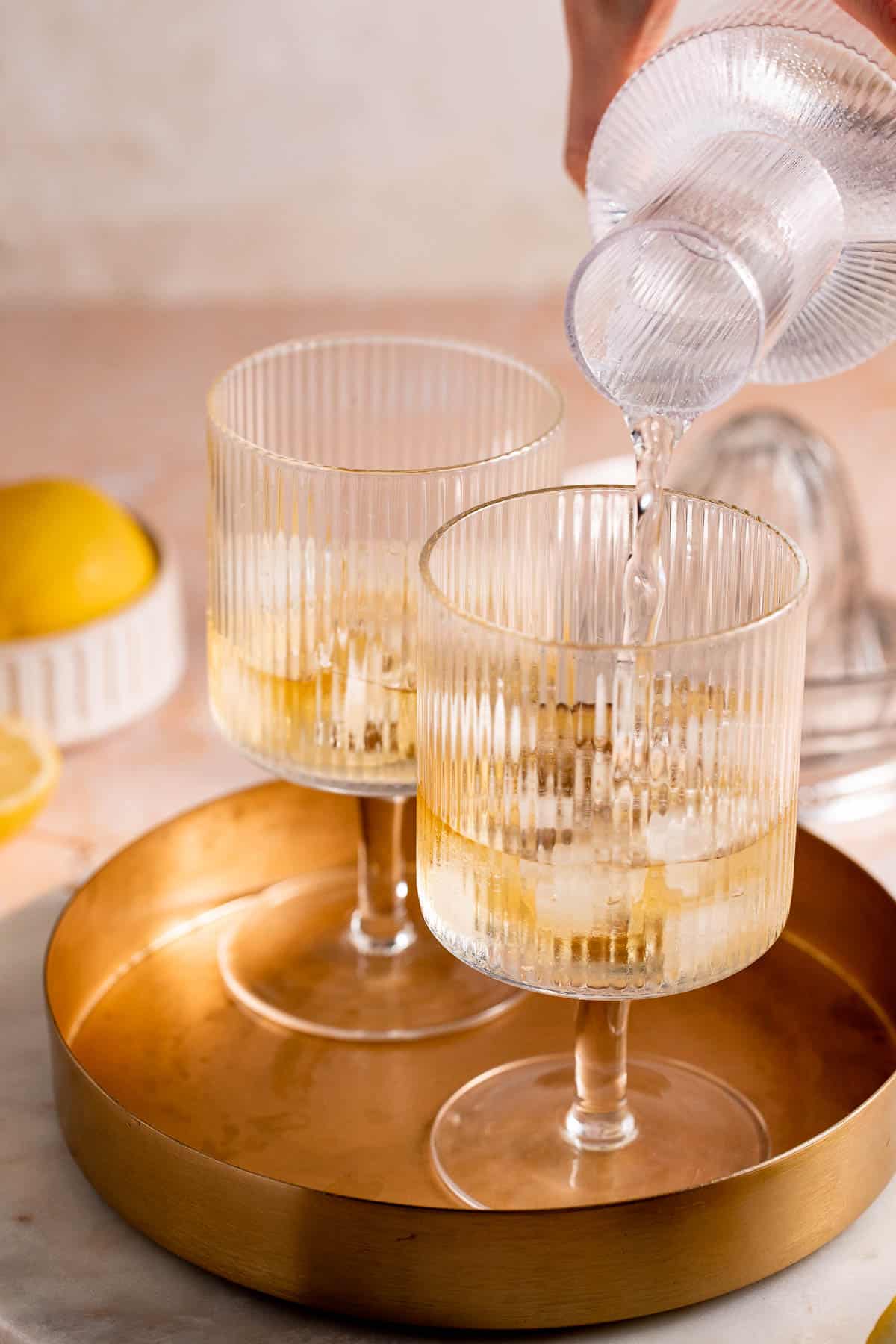 Bubbly water pouring into a serving glass on a gold tray.