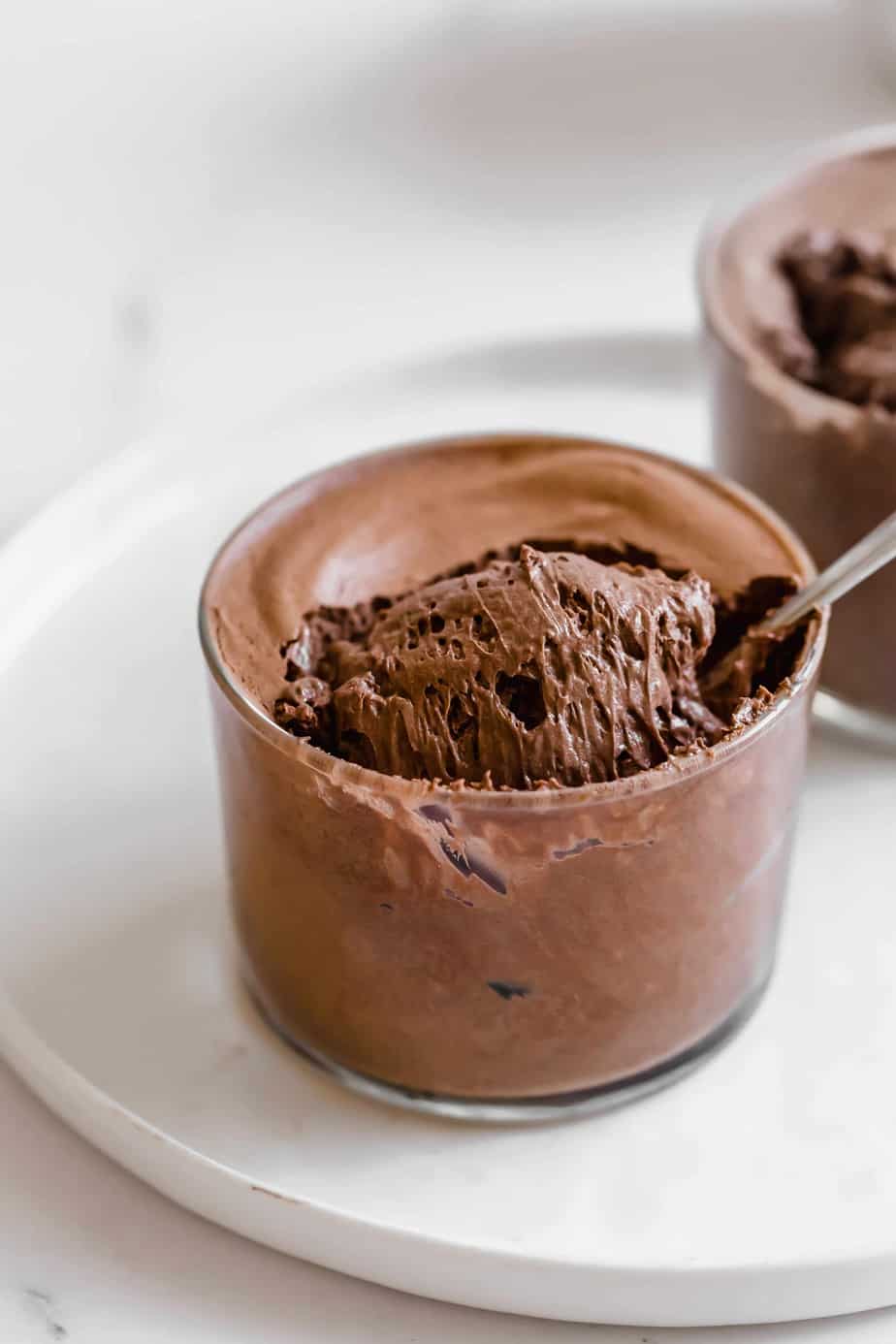 A glass of chocolate mousse with a teaspoon in it.