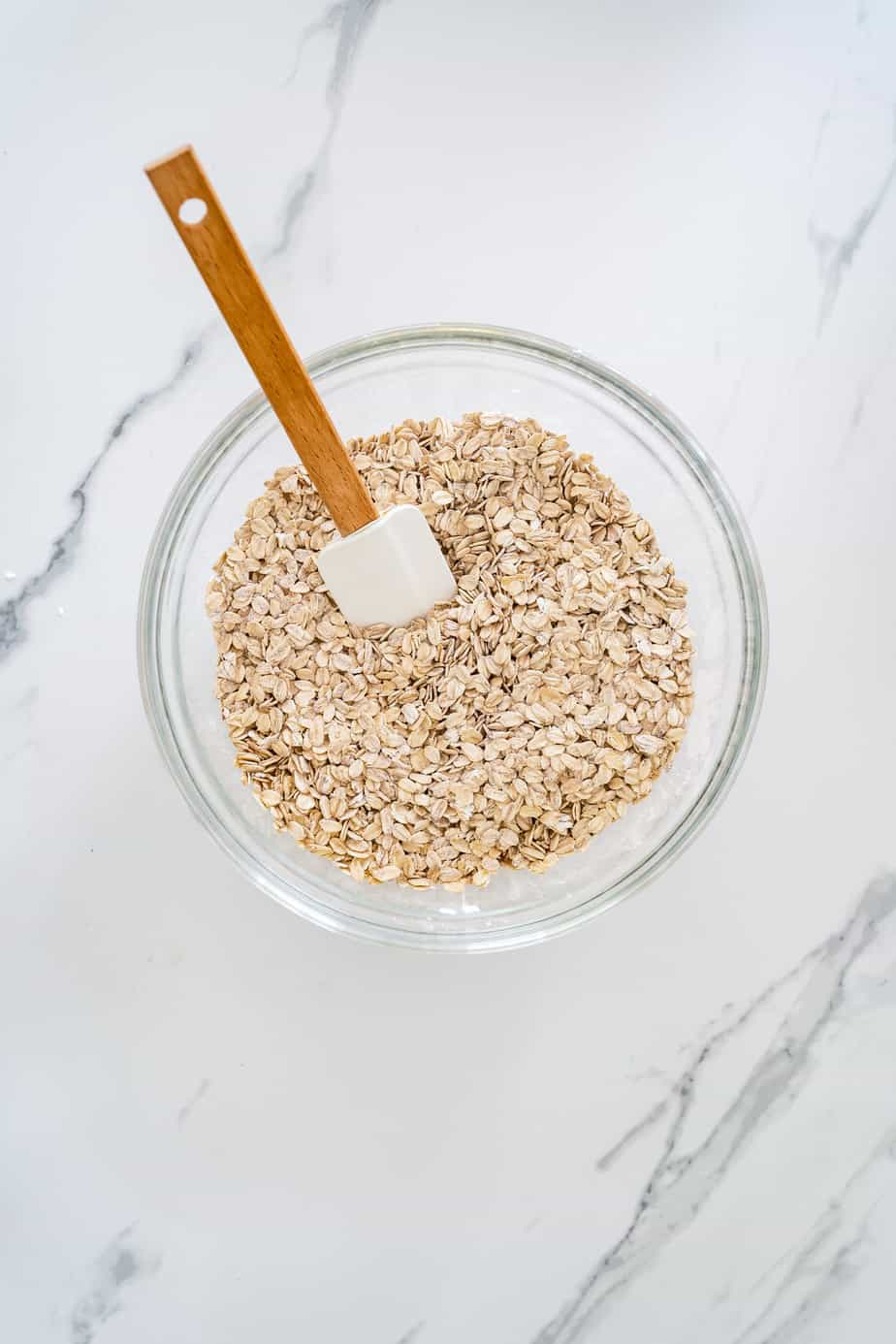 A mixing bowl with rolled oats and a spatula.