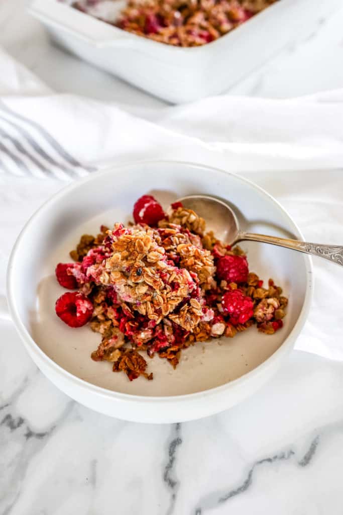 A white bowl of baked raspberry oatmeal with a silver spoon.
