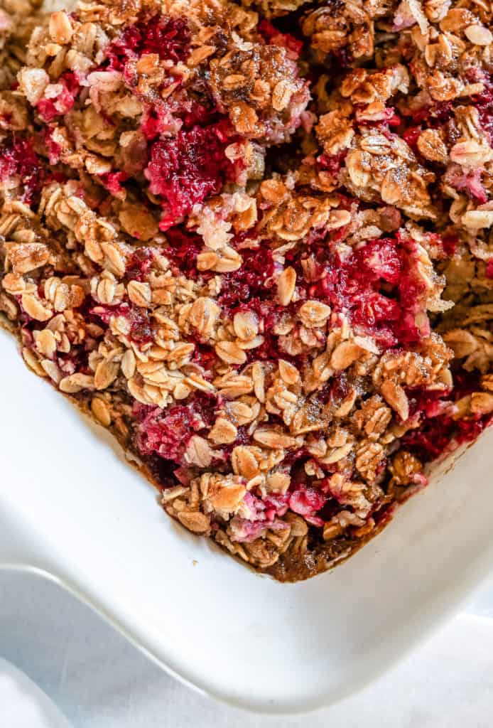 A white dish of baked oatmeal with red raspberries.
