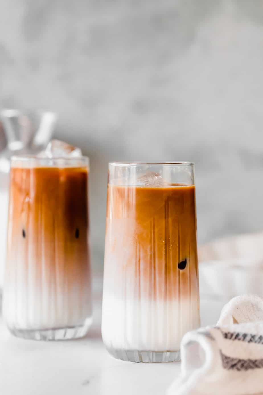 Two iced coffee drinks in glasses served with ice.