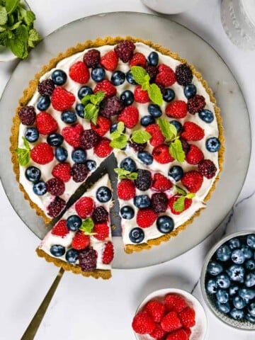 summer berry tart with marble board, fresh berries and gold cake lifter