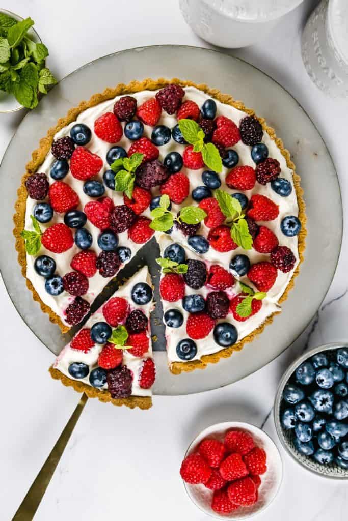 summer berry tart with marble board, fresh berries and gold cake lifter