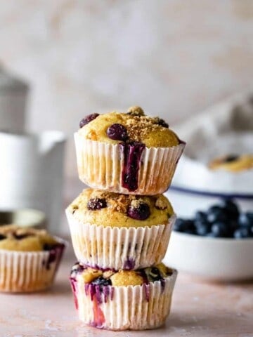 Blueberry muffins stacked on top of each other with blueberries in the background