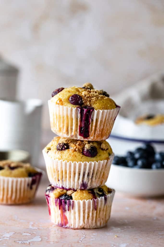 Blueberry muffins stacked on top of each other with blueberries in the background