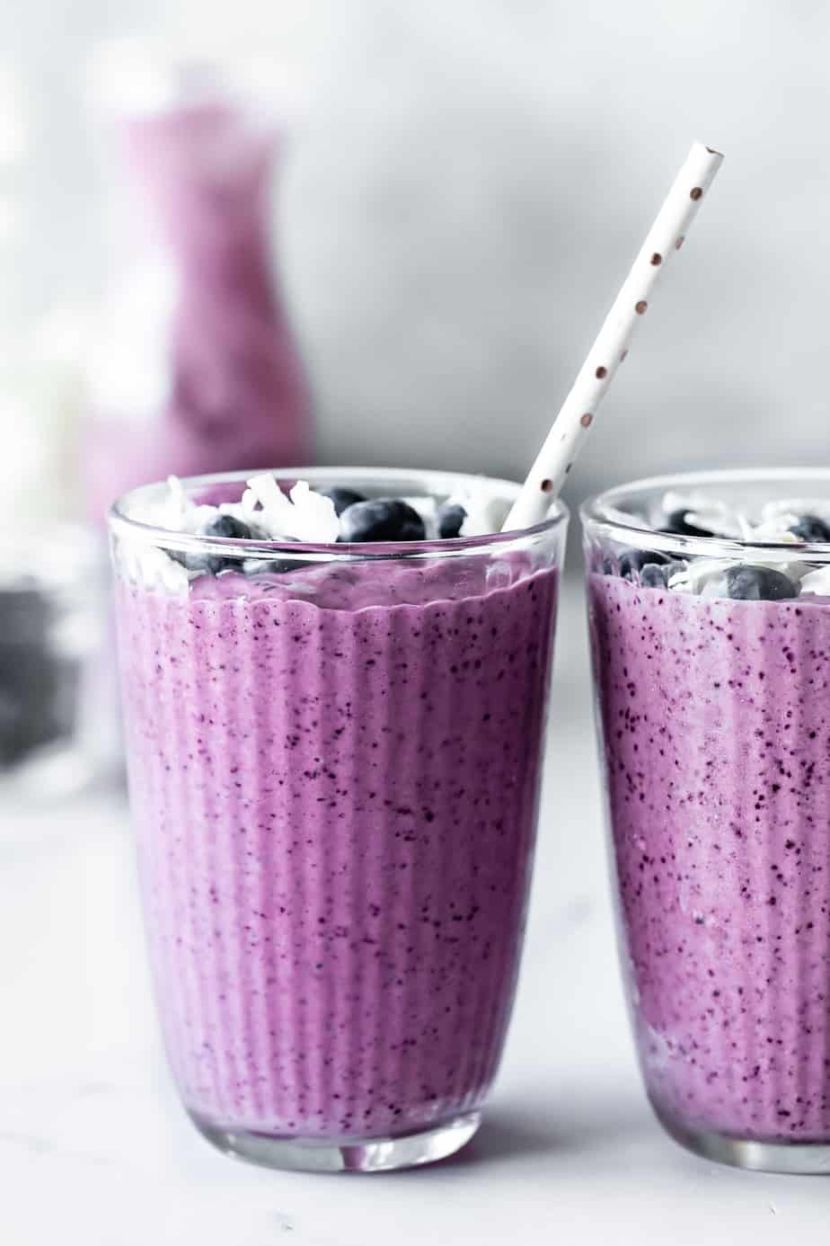 Two pineapple and blueberry smoothies in glasses with straws and fresh blueberries.