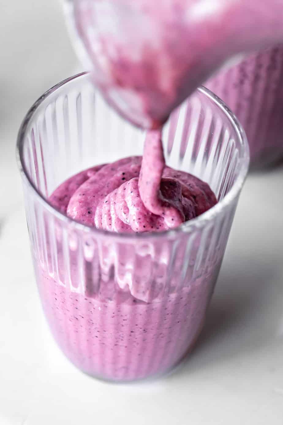 Pouring a blueberry smoothie into a glass.