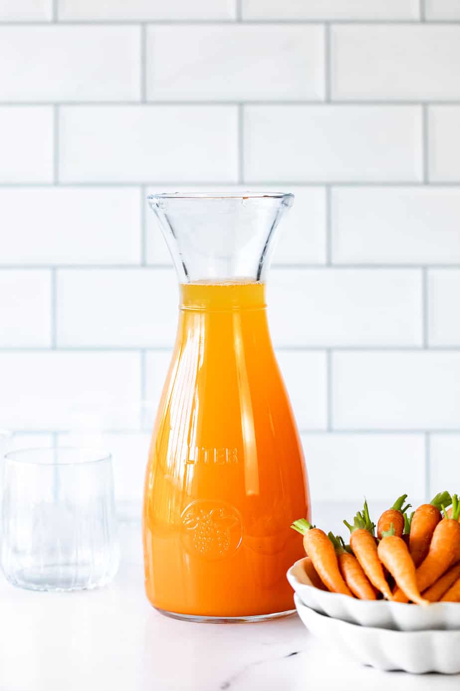 A glass canister of carrot juice with fresh carrots